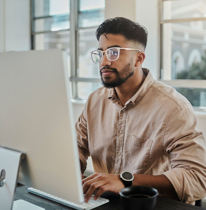 Man wearing glasses working at a desktop computer in a bright office environment