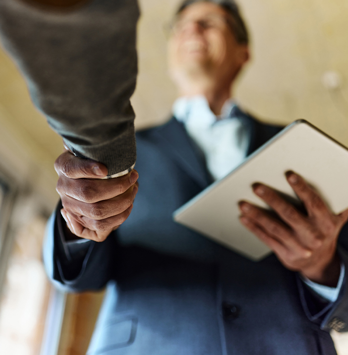 A salesman in a suit shaking hands with another person, holding a tablet, symbolizing a successful business agreement
